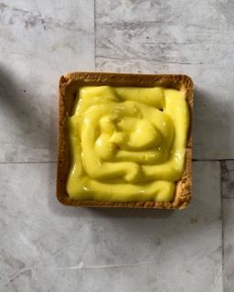 Un contenitore quadrato pieno di salsa gialla su un tavolo.