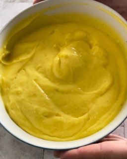 Una persona tiene in mano una ciotola di salsa gialla.