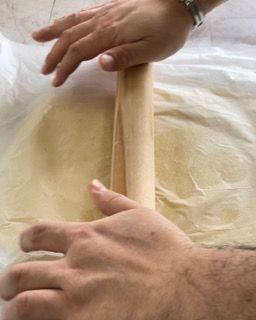 Una persona sta stendendo la pasta con un mattarello di legno.