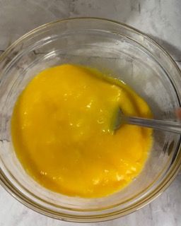 Una ciotola di vetro piena di liquido giallo e un cucchiaio dentro.