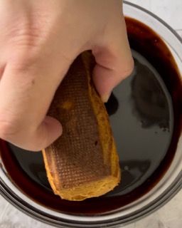 Una persona tiene in mano un pezzo di cibo in una ciotola piena di liquido.