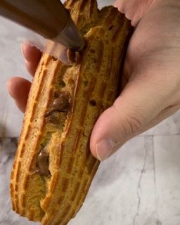 Una persona tiene in mano un dolce ricoperto di glassa al cioccolato.