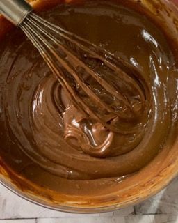 Una ciotola di glassa al cioccolato con una frusta dentro.