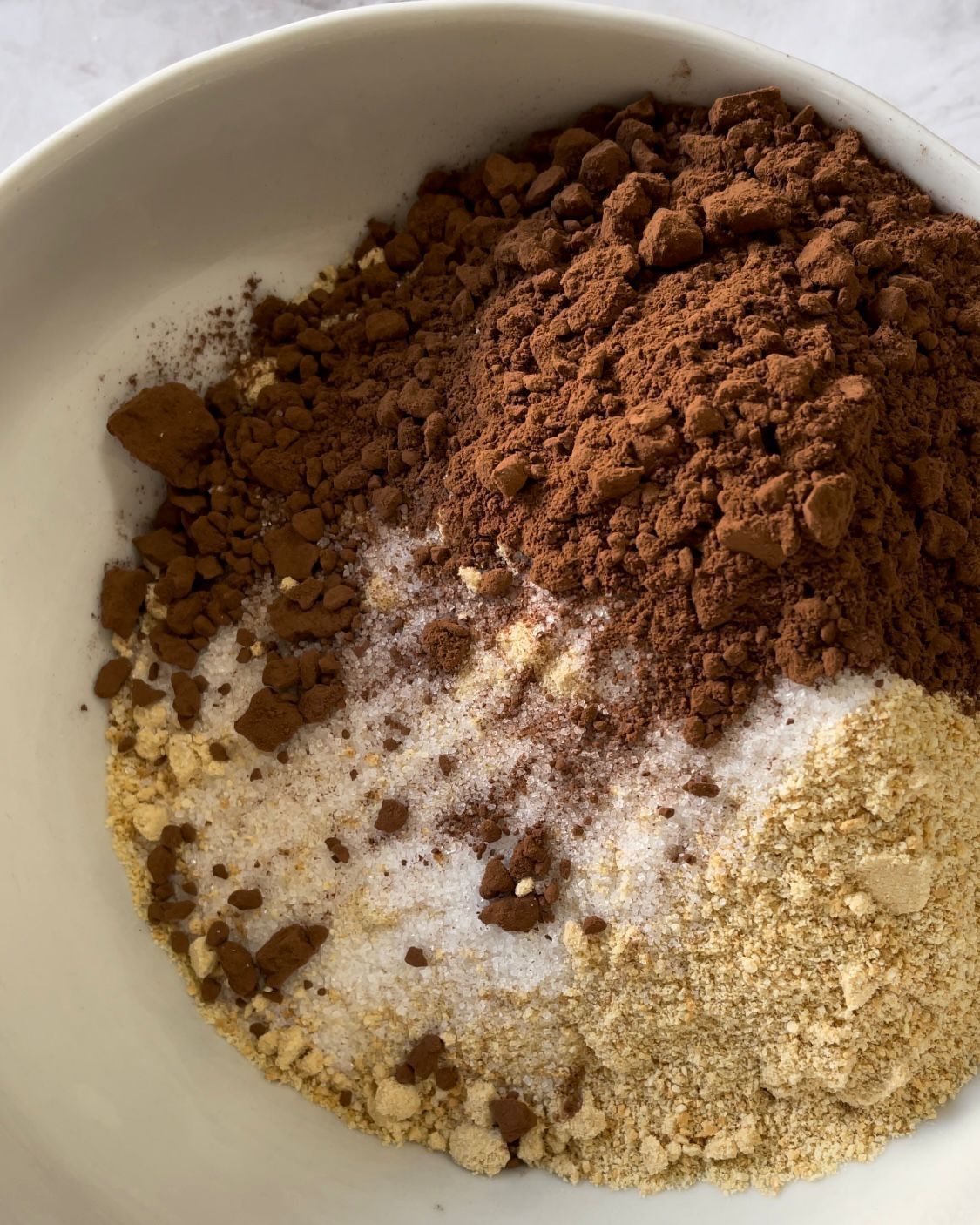 Una ciotola bianca piena di vari ingredienti tra cui il cacao in polvere