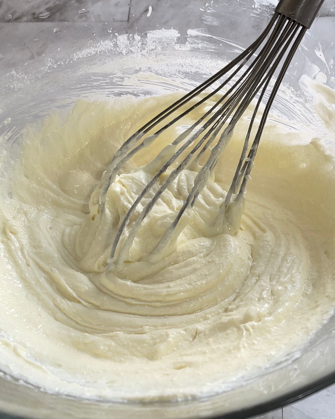 Si usa una frusta per mescolare un impasto in una ciotola di vetro.