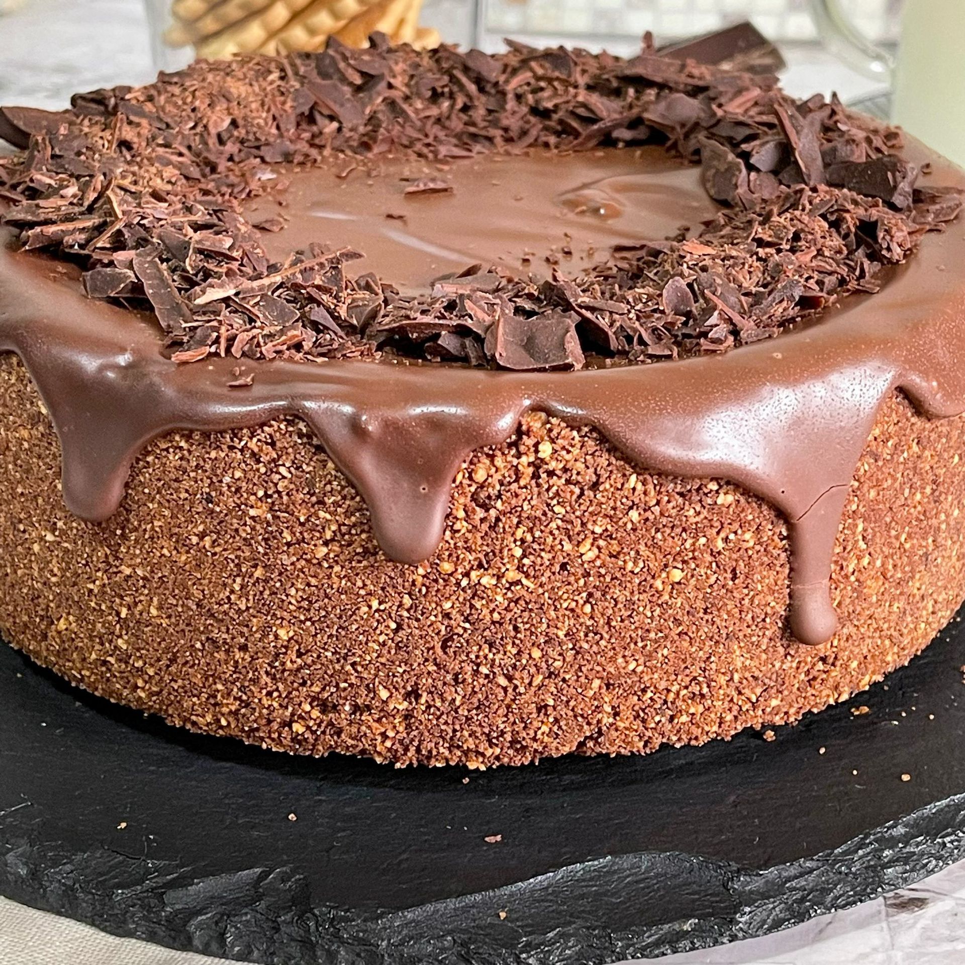 Una torta al cioccolato con scaglie di cioccolato sopra è appoggiata su un piatto nero.