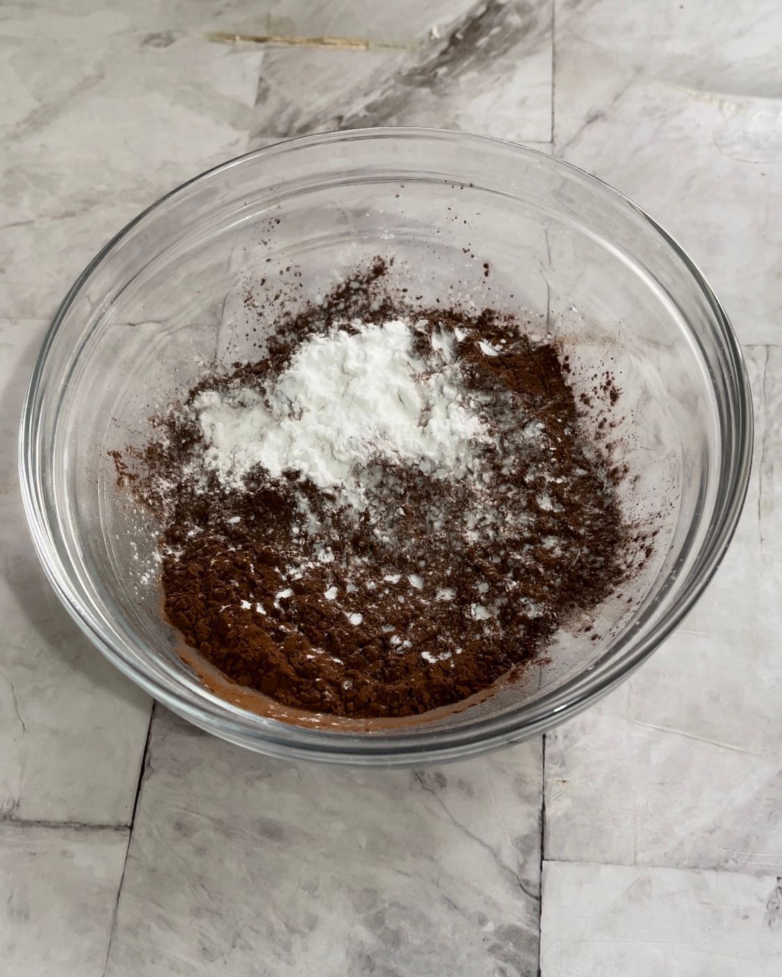 Una ciotola di vetro piena di cioccolato e farina su un tavolo.