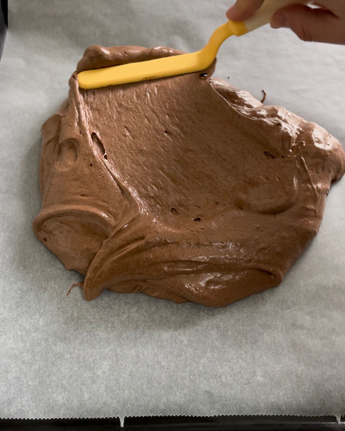 Una persona sta spalmando la glassa al cioccolato con una spatola