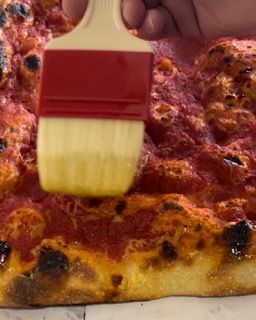 Una persona sta applicando la salsa su una pizza con un pennello