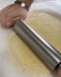 Una persona sta stendendo un pezzo di pasta con un mattarello.