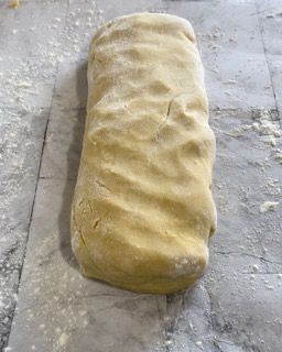 Un pezzo di pasta è appoggiato su un tavolo ricoperto di farina.