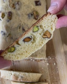 Una persona tiene in mano un pezzo di pane con sopra dei pistacchi.