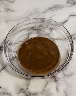 Una ciotola di vetro piena di liquido marrone su una superficie di marmo.