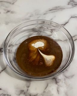 Una ciotola di vetro piena di liquido marrone su una superficie di marmo.