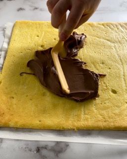 Una persona sta spalmando la glassa al cioccolato su una fetta di torta con un cucchiaio di legno.