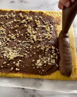 Una persona sta spalmando la glassa al cioccolato su una fetta di torta.