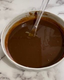 Una ciotola di salsa al cioccolato con un cucchiaio dentro su un tavolo.