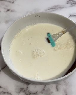 Una ciotola di liquido bianco con una spatola blu dentro.