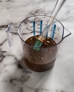 Una tazza graduata piena di liquido marrone e un cucchiaio