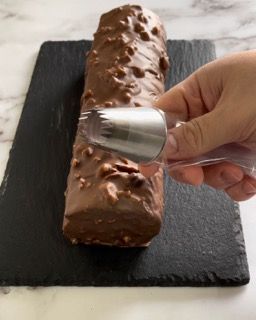 Una persona sta glassando una torta al cioccolato con un beccuccio per dolci