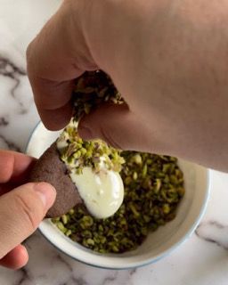 Una persona sta immergendo un biscotto in una ciotola di pistacchi e panna.