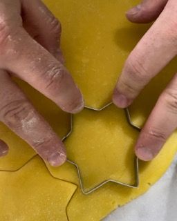 Una persona sta usando un tagliabiscotti a forma di stella su un pezzo di pasta.