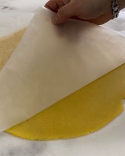 Una persona tiene in mano un pezzo di carta oleata sopra un pezzo di pasta gialla.