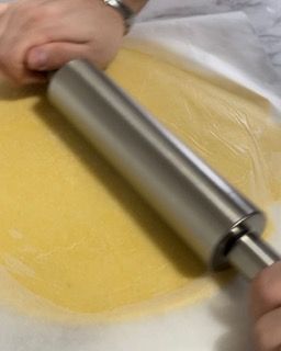 Una persona sta stendendo un pezzo di pasta con un mattarello.