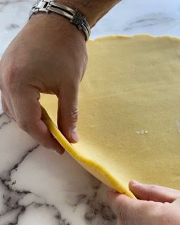 Una persona tiene in mano un pezzo di pasta su un tavolo.