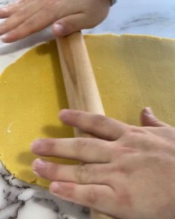 Una persona sta stendendo un pezzo di pasta con un mattarello.