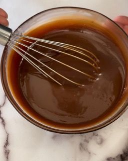 Una ciotola di liquido marrone con una frusta dentro