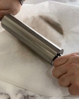 Una persona sta stendendo la pasta con un mattarello su un pezzo di carta oleata.