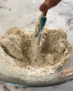 Una persona sta mescolando la farina in una ciotola di vetro con una spatola.