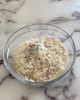 Una ciotola di vetro piena di un composto di farina e acqua su un tavolo.