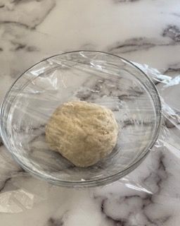 Una palla di pasta è avvolta nella pellicola trasparente in una ciotola di vetro.