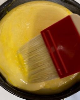 Un pennello rosso viene utilizzato per stendere un liquido giallo in una padella