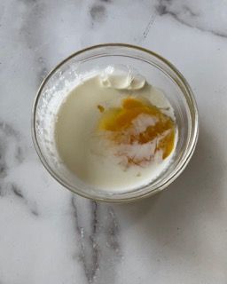 Una ciotola di vetro piena di yogurt e miele su una superficie di marmo.