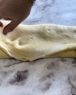 Una persona tiene in mano un pezzo di pasta su un tavolo.