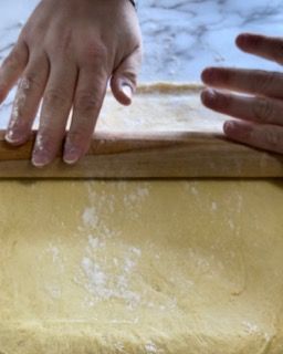 Le mani di una persona sono su un pezzo di pasta su un tagliere