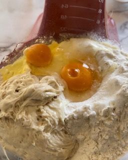 Una ciotola di farina con le uova dentro e un misurino sullo sfondo.