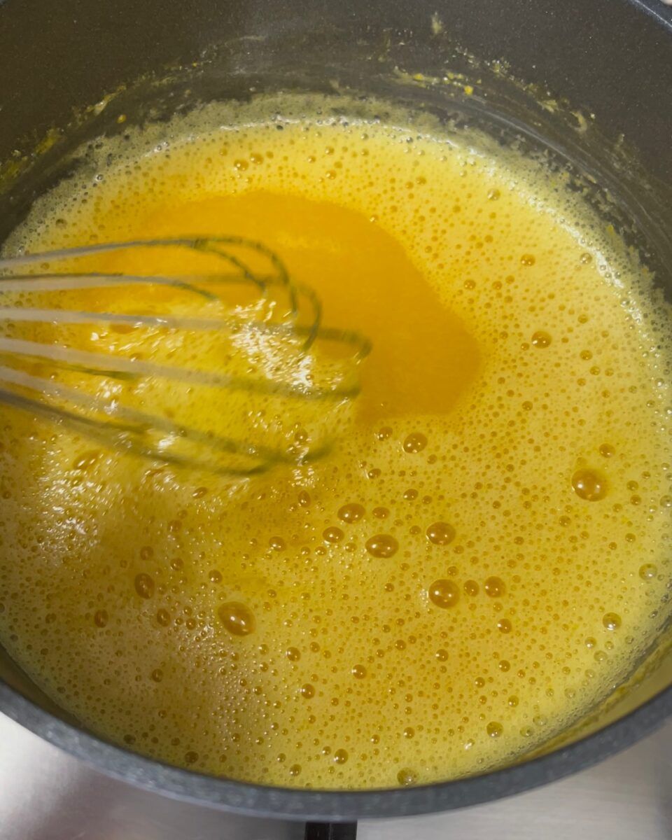 Una frusta mescola un liquido giallo in una pentola.