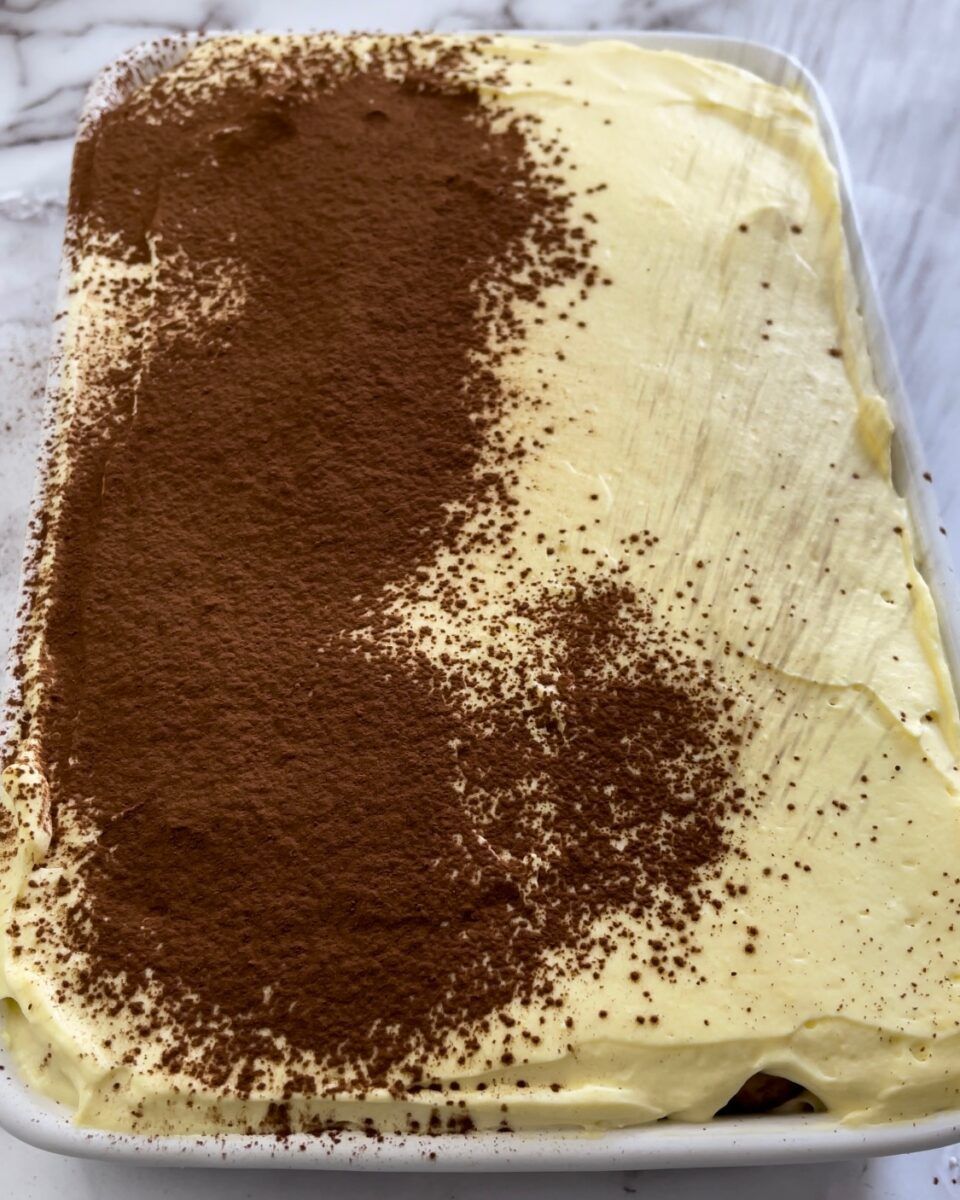 Una pirofila bianca piena di tiramisù classico spolverato con cacao