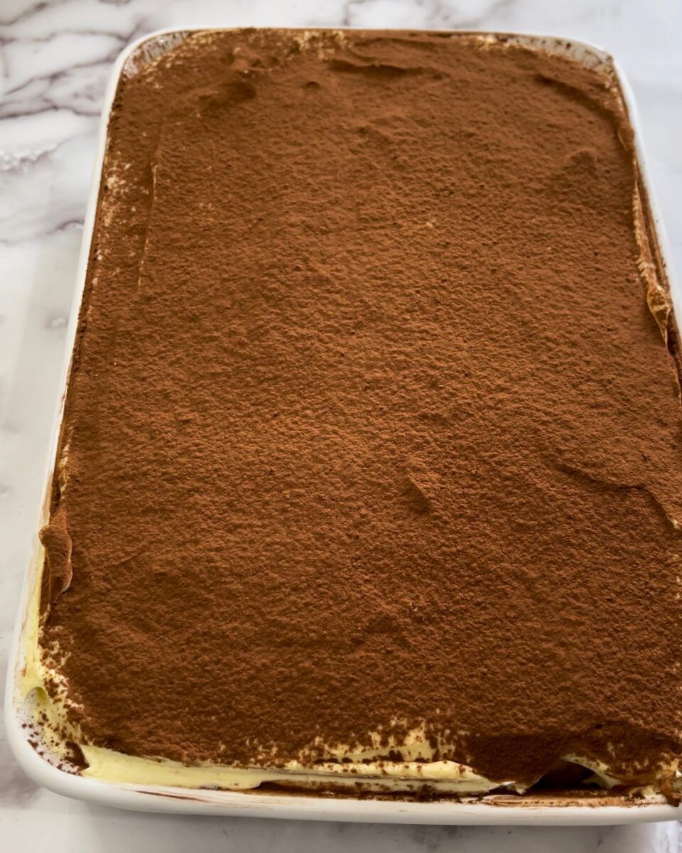 Una pirofila bianca piena di tiramisù classico spolverato con cacao