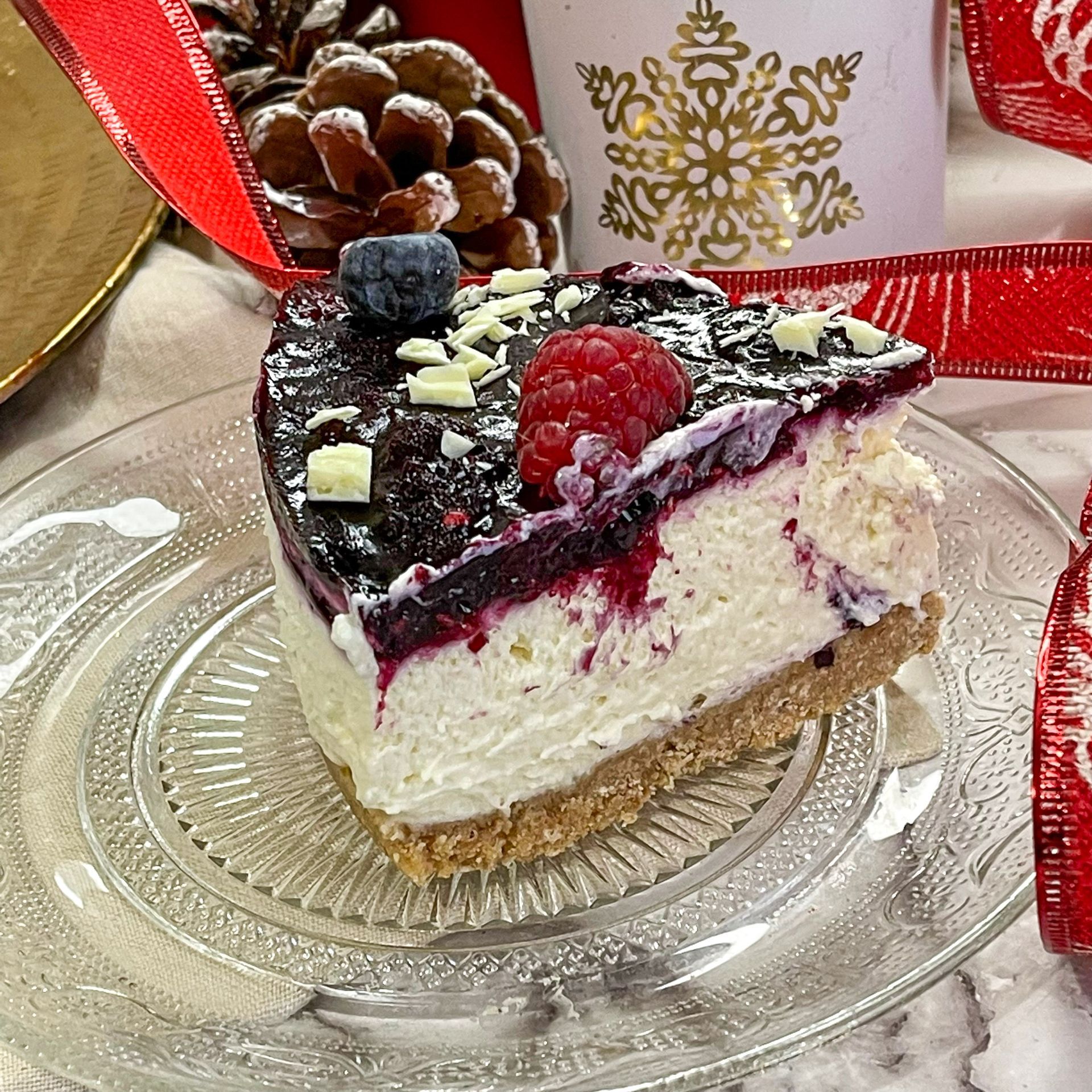 Una fetta di cheesecake con lamponi e mirtilli su un piatto di vetro.