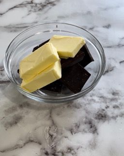 Una ciotola di vetro piena di cioccolato e burro su un tavolo.