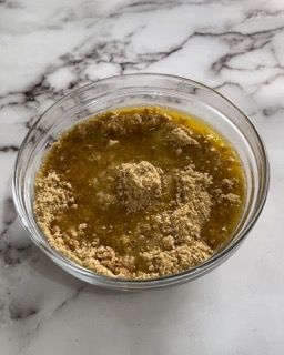 Una ciotola di vetro piena di un liquido giallo e polvere marrone su un tavolo.