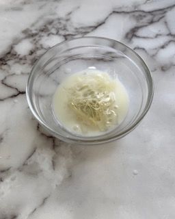 Una piccola ciotola di vetro piena di un liquido bianco su una superficie di marmo.