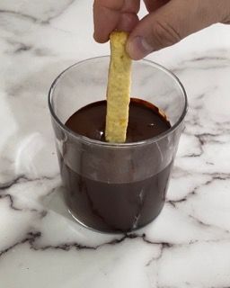 Una persona che immerge una patatina fritta in una tazza di salsa al cioccolato