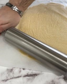 Una persona sta stendendo la pasta con un mattarello.