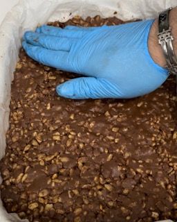 Una persona che indossa guanti blu tiene in mano un pezzo di torta al cioccolato.